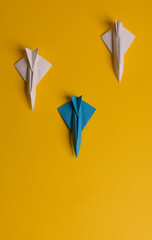 Group of paper plane in one direction and with one individual pointing in the different way on yellow background. Christmas ttrip. Presents and gifts.