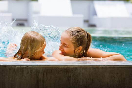 Happy people have fun at pool side edge. Funny photo of young mother with child relaxing in outdoor swimming pool. Family lifestyle, kids water sport activity with parents on summer holiday