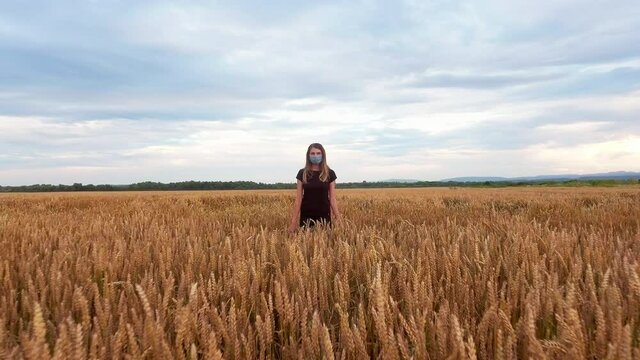 The girl in a mask from a virus, stands in a wheat field, the camera flies back from the girl back. Shows loneliness of the person in a coronavirus