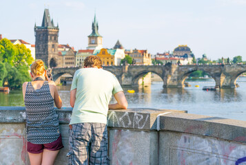 Male and female, a couple by the bridge standing and taking photographs with dslr camera of charles bridge in Prague.Chzech republic..