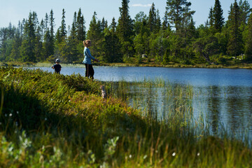 Fototapeta na wymiar A young girl with her little brother fishes in a small lake. Shot in the deep wild forest of Hallingdal, Gol, Norway.