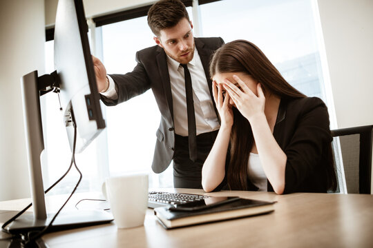 Conflict, Crisis And Dismissal At Work. Young Businessman Yells At Subordinate Female Assistant After Her Failure. Businessman Points At Monitor And Fires Worker. Resolving A Serious Work Problem.