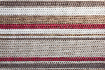 Texture of a textile rug with stripes in red and tons of brown.