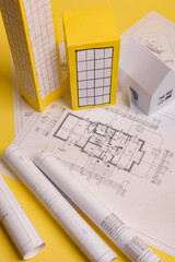 White family paper house, house projects plan and blueprints in the background. Minimalistic and simple concept, style. Horizontal orientation. View from above