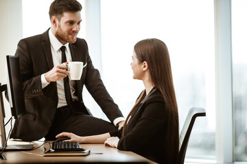 Flirt and relations at work. Smiling male businessman sits and shows sexual interest to positive minded female assistant at workplace. Two people man and woman love and sympathy in modern office