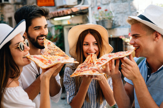 Happy group of people eating pizza outdoors,they are enjoying together.