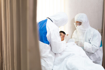 Naklejka premium Two medical technicians wearing full protective equipment collected samples from Asian young man lying in a hospital bed, the operation of the coronavirus mobile testing unit.