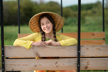 Obraz premium Beautiful teen girl looking at the camera. Happy smiling girl sitting in a wooden carriage of rickshaw and looking at the camera. Asia travel concept. Wooden alcove.