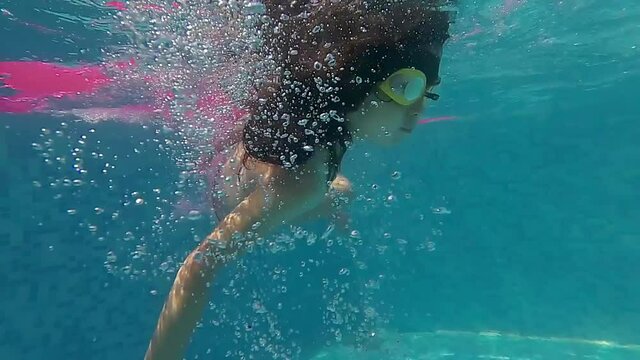 The girl sits on a rubber mattress in the pool, rolls over and starts swimming underwater