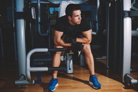 Full length portrait of young athlete seated on gym equipment and taking a break after workout