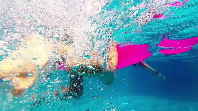 Slow motion footage of two girls swimming, holding on to a pink rubber mattress, underwater shot