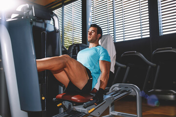 Young athletic man working his quads at machine press in the gym
