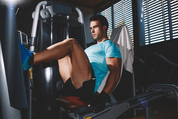 Fototapeta na wymiar Side view of young handsome man doing leg presses in health fitness center