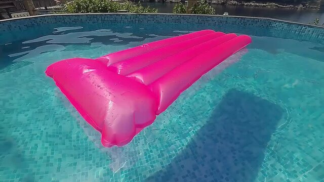 A pink rubber mattress floats in the middle of a small pool