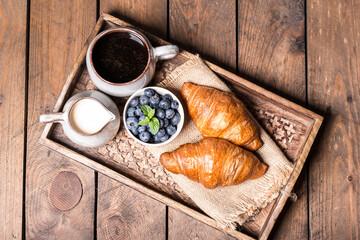 romantic breakfast with fresh croissants coffee,milk and berries on wooden table