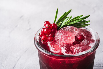 Fresh ice cold fruit cocktail in glass, refreshing summer red currant berry drink with rosemary leaf on stone concrete background, angle view macro