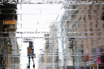 Blurry reflection shadow silhouette on wet street of a woman walking on a rainy day - 370785517