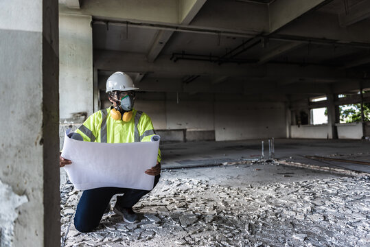 Black People Construction Worker Wearing Face Mask And Safety Helmet While Looking To An Area Follow Drawing On Construction Site. Civil Engineering Or Surveyor Checking In The Demolished Building.