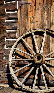 Old West Aged Rusty Wooden Wagon Wheel Leaning up Against a Log Cabin Wall