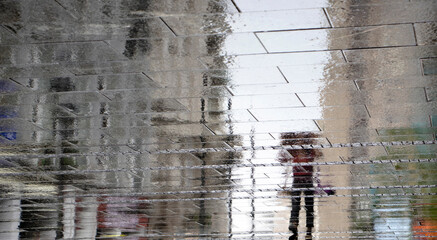 Blurry reflection shadow silhouette on wet street of a woman walking on a rainy day