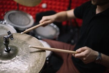 Male hands with drumsticks playing drum set. Cropped male drummer holding wooden drumsticks and...