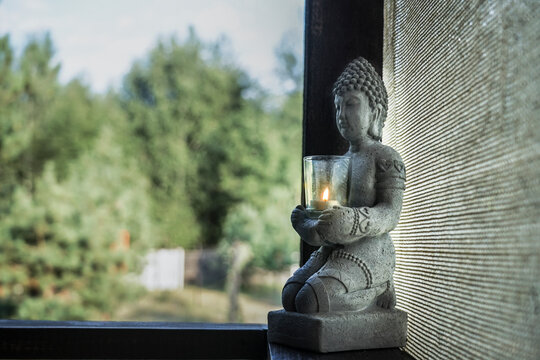 statue of a buddha with a candle stand on a wooden windowsill