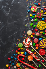 Colorful lollipops, marmalade and colored round candies on a black stone background. Children's holiday sweets. Top view, flat lay,copy space.