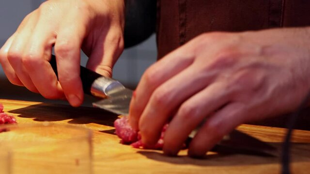 Restaurant kitchen from the inside - chef cutting meat in small pieces with sharpened knife