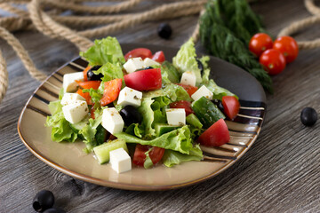 Greek salad on a striped plate on the table in the cafe