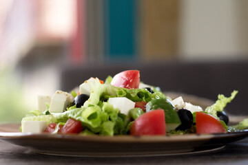 Greek salad on a striped plate on the table in the cafe