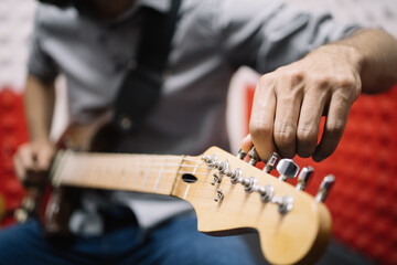 Cropped musician tuning guitar in music studio. Cropped and out of focus guitar player adjusting...