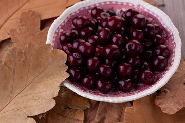 ripe cherry in close-up on a vintage plate against the background of autumn leaves. Top view. Copyspace