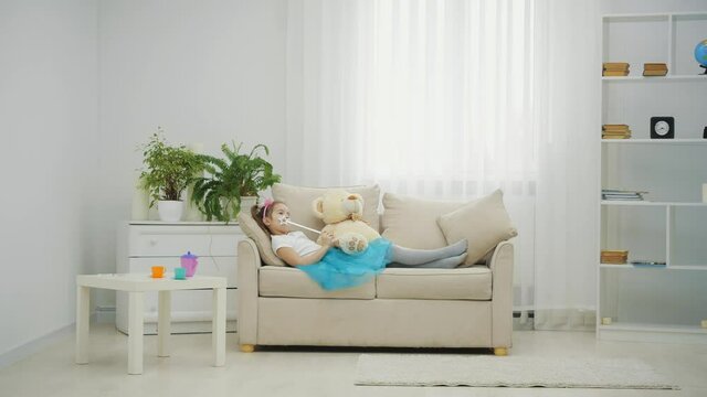 Little fairy lying on the sofa with magic wand in her hand and teddy bear sitting near her.