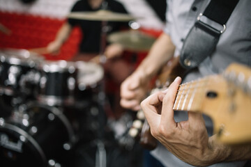 Selective focus image of band playing music instruments. Blurred and unrecognizable musicians playing guitar and drum set in studio.