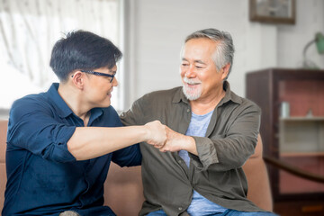 Cheerful senior asian father and middle aged son fists bumping, mature aged dad and millennial man sitting on couch in living room at home, Happiness Asian family concepts