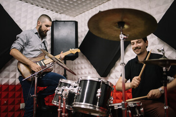 Smiling musicians playing guitar and drums. Happy music band members enjoying playing instruments in music studio.