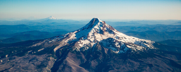 A summer aerial shot of Mt Hood with much of its snow melted and showing layered hills and Mt Jefferson in background