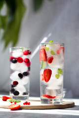 tall glasses full of ice and frozen strawberries and blueberries inside with mint leaves in the sun