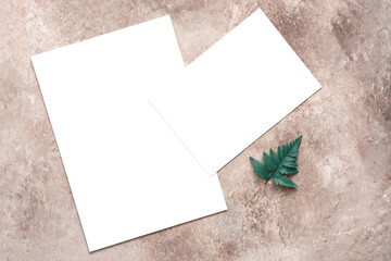 Blank paper mockup and fern leaves on beige grunge background. Modern tropical stationery still life. Template for invitation and greeting cards.. Top view, flat lay, copy space.