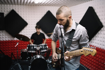 Fototapeta premium Electric guitar player and drummer behind the drum set. Rock band working in music recording studio with sound speakers.