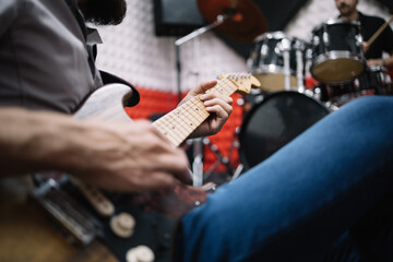 Close-up view of cropped man playing guitar. Cropped guitar player sitting on ground next to blurred drummer.