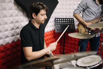 Handsome man playing with drumsticks while sitting in recording studio. Musician playing with drumsticks while sitting at drum set in music studio.