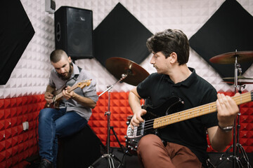 Band of adult musicians rehearsing in studio. Bass guitar player, electro guitar player playing near drum set in music studio.