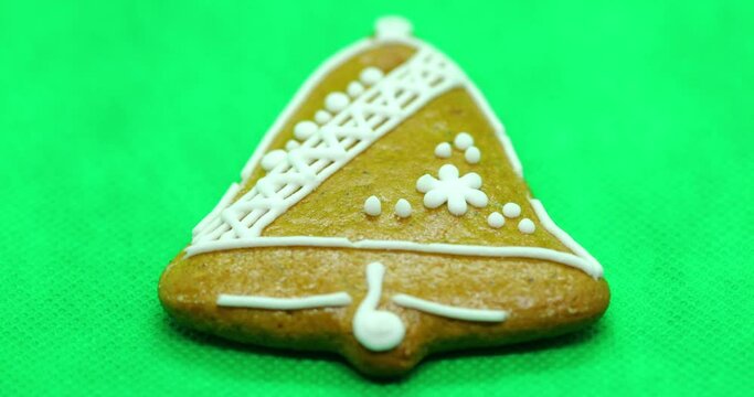 Zoomed in a gingerbread pastry with white decorations on top in the shape of a Christmas bell on a green background.