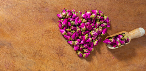 Dried pink rose tea for brewing on a wooden table