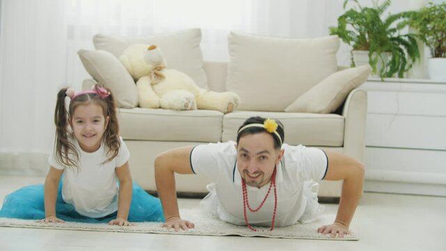 Funny father and daughter wearing nice headgears, going push-ups, on the carpet.