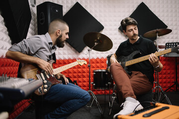 Guitar players rehearsing while sitting in recording studio. Focused male guitarists playing guitars in soundproof studio.