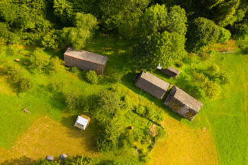 Aerial drone view of old wooden hut on mountain slope. Stable for cattle and barn near hut, green well-groomed yard