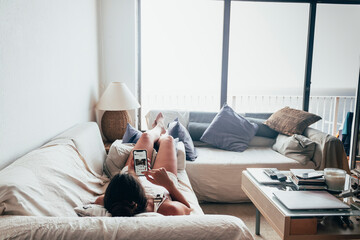 Girl lying on the couch checking her cell phone at her vacation home with views to the sea