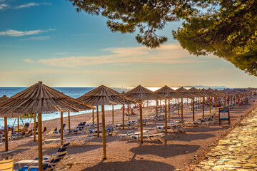 Beach with straw umbrellas at sunset near Primosten town, a popular tourist destination on the Dalmatian coast of Adriatic sea in Croatia, Europe.